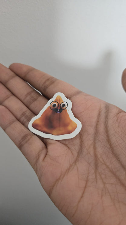 Hand holding a sticker of a cartoon samosa with googly eyes against a neutral background