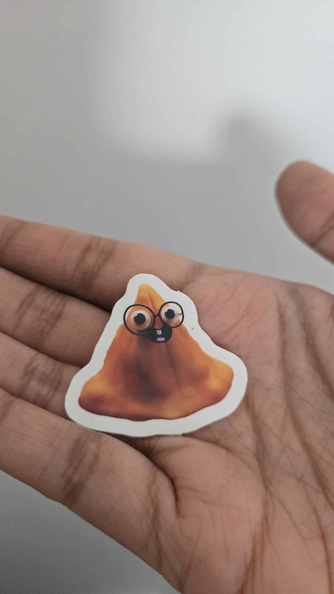 Sticker of a cartoonish samosa with glasses held in a hand against a neutral background